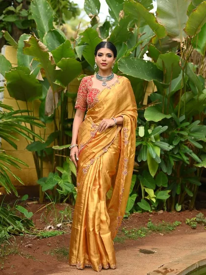Experience the royal glow of this handwoven tissue Kanjivaram silk saree in a stunning gold shade. I paired it with a contrasting red blouse, heavily embroidered with multi-colored threadwork, creating a statement piece for those who appreciate rare collections with a regal touch.