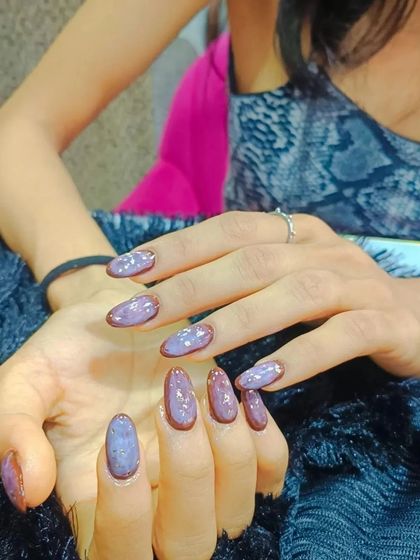 A unique design with a speckled purple polish and a brown border around each nail.