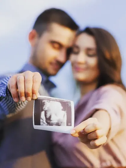 A classic maternity announcement photo. This couple shares their joy by holding up their baby's first picture, the ultrasound scan, in a beautifully composed outdoor shot.
