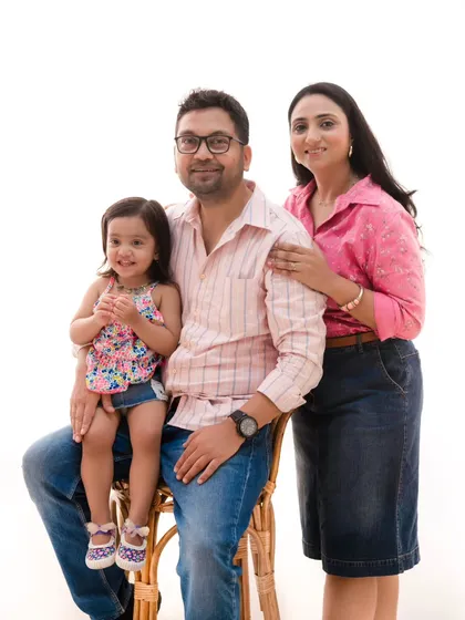 A classic seated portrait. The use of a simple rattan chair and a clean background keeps the focus entirely on the family's warm smiles and connection.