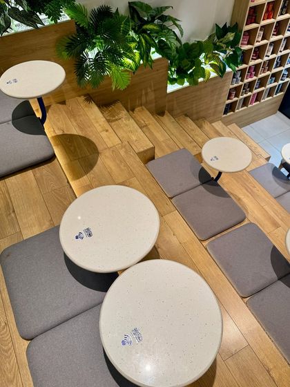An overhead shot of the casual seating at Beanly. The small, round tables and floor cushions on the wooden steps create a relaxed, coffee-shop vibe, encouraging patrons to settle in.