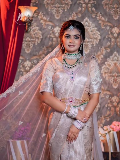 A model dressed in a stunning silver tissue saree with a sheer veil, paired with a modern emerald and diamond necklace set.