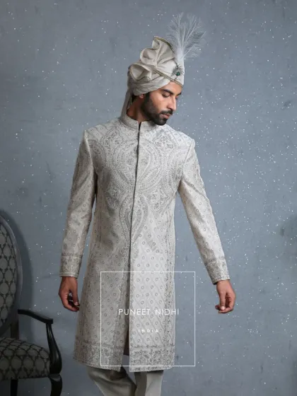 A side profile of the ivory silk sherwani, showing how the resham embroidery with paisley and floral patterns cascades down the length of the garment, paired with a matching ivory silk turban.