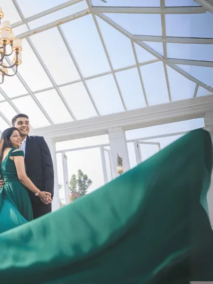 A dynamic shot capturing the movement of the bride's flowing green dress inside a bright conservatory. The angle and motion add energy and life to the portrait.