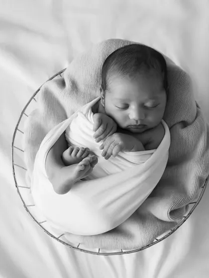 An overhead black and white view of a swaddled newborn in a basket. This perspective highlights how tiny and perfectly bundled they are.