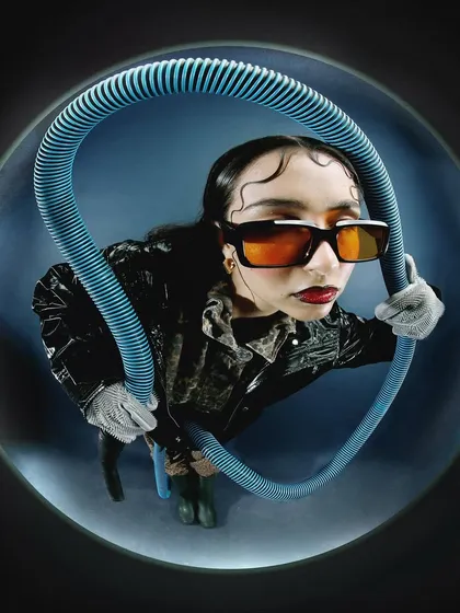 A creative portrait using a blue corrugated tube to frame the model's face. This use of an unconventional prop is a hallmark of experimental art direction.