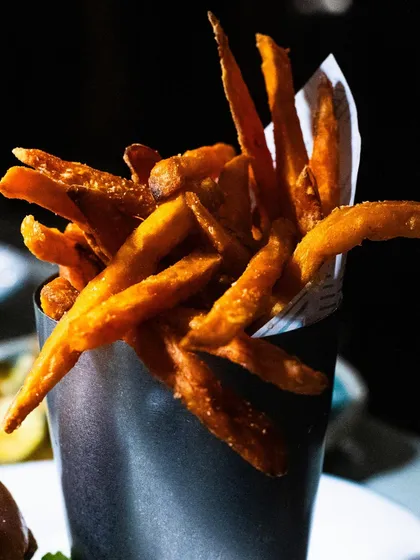 A cone of crispy sweet potato fries, shot with dramatic lighting to make them look like the star of the show.