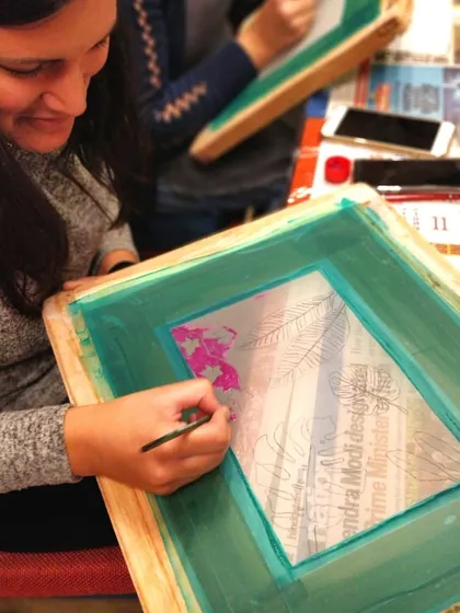 A student carefully preparing her screen for a silkscreen print, painting the blocking fluid around her design.