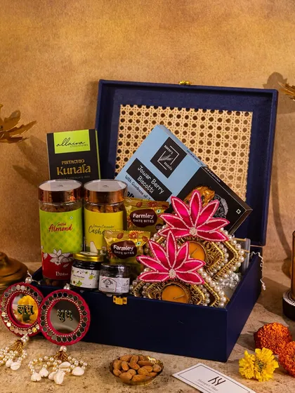 A sophisticated navy blue hamper for Diwali, featuring a cane-work lid. The styling with lotus-themed decor and scattered almonds adds a touch of elegance and texture.