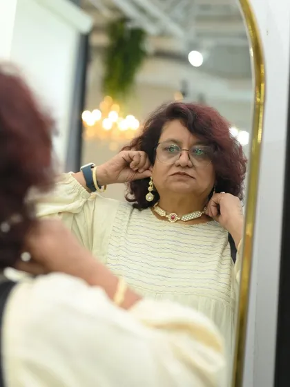 A client admiring her new look in the mirror, trying on a pearl choker and matching earrings.