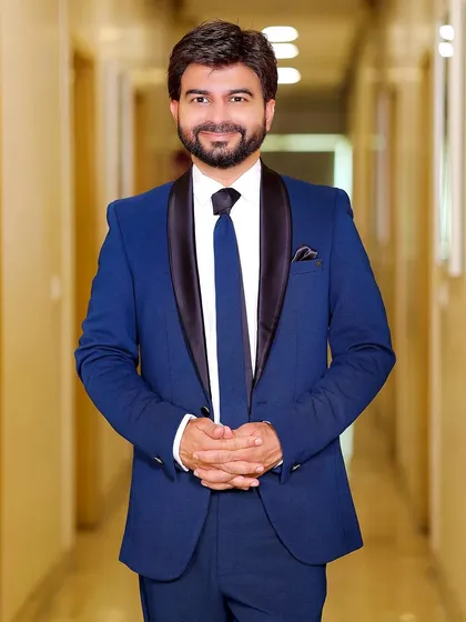 A classic, welcoming portrait of the groom. His hands are clasped and he has a warm smile, ready for the big day.