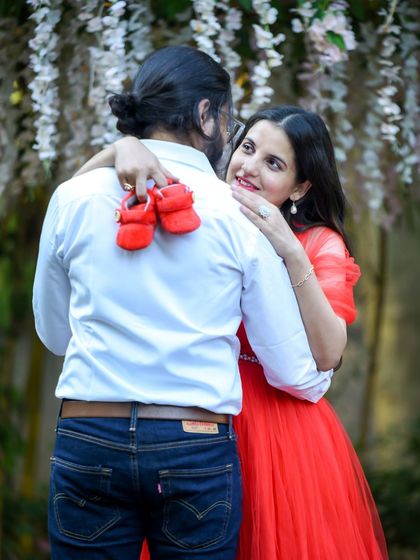 A close-up of a tender moment between a couple, with the focus on the tiny red baby shoes they are holding.