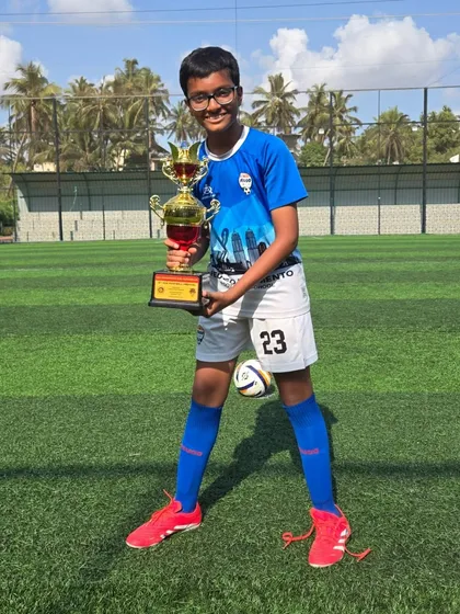 A U14 player with his foot on the ball, posing with his trophy.