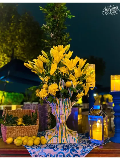 This centerpiece for a Sicilian-themed dinner features yellow lilies bursting from a unique, face-sculpted vase. It’s an example of how I use artistic details to elevate the theme and create talking points at every table.
