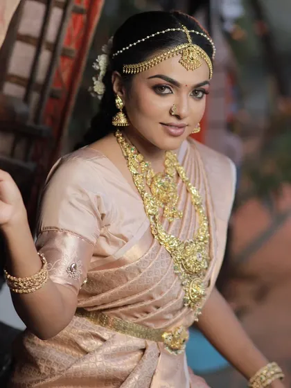 A stunning shot of a model in a light-colored silk saree with heavy gold jewelry, showcasing a classic and regal muhurtham look.