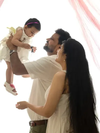 A bright, high-key family portrait. The soft pink curtains add a delicate touch to this joyful and light-filled image.