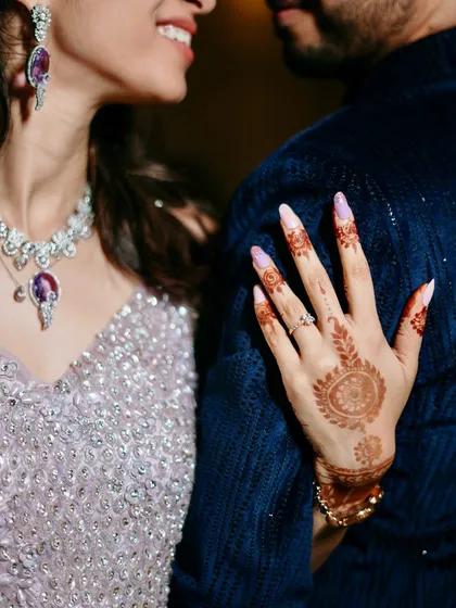 A close-up detail shot of the bride's hand on the groom's shoulder. This image highlights her beautiful henna, engagement ring, and stunning jewelry.
