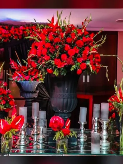 A close-up of the floral decor for a red-themed sangeet. The arrangement includes a lavish display of red roses and anthuriums on a mirrored table, adding to the luxurious feel.
