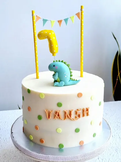 A simple and sweet dinosaur cake with a polka dot design. The topper features a cute dinosaur holding a number one balloon.