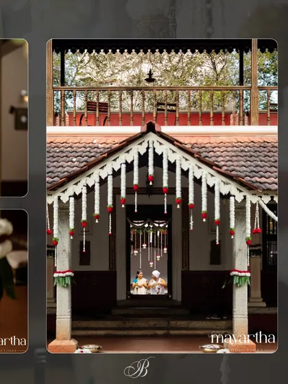 A stunning frame-within-a-frame shot, looking through the decorated entrance of a traditional South Indian house towards the Vara Puje ceremony. The floral decor on the eaves perfectly frames the moment.