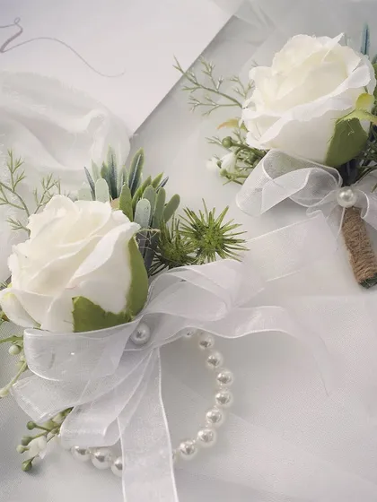 It's all in the details. This set features a classic white rose wrist corsage with a pearl bracelet for the mothers of the bride and groom, perfectly paired with a matching boutonniere for the fathers. These small touches make your closest family feel special and included.