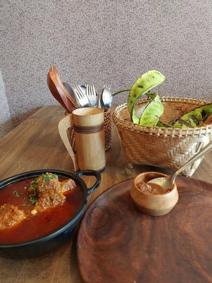 A hearty meat curry served in a traditional pot with bamboo utensils. This image captures the rustic and authentic essence of our food.