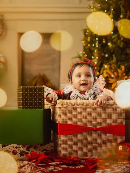 The best present of all. A baby peeking out of a basket surrounded by Christmas gifts and warm lights.