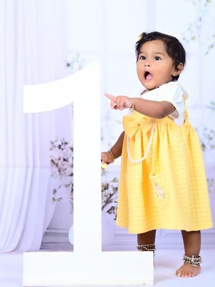 A little girl standing next to a large number "1" prop, celebrating her first birthday.