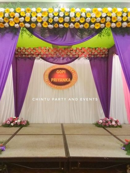 A wedding mandap decoration with purple and yellow drapes. The stage is adorned with fresh flower arrangements for a traditional look.