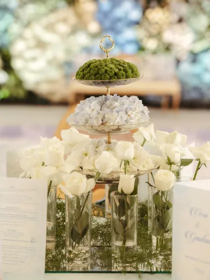 A unique centerpiece featuring a three-tiered stand with floral arrangements on each level, surrounded by single white roses in individual glass vials.