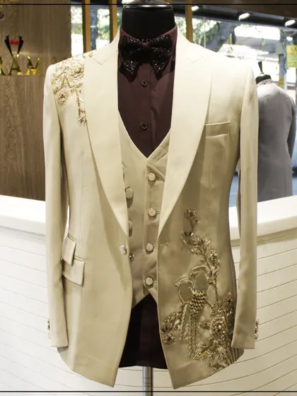 An off-white three-piece tuxedo with stunning gold bird and floral embroidery. This is a regal and eye-catching choice, perfect for a groom's reception outfit.