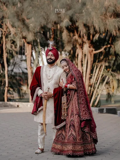 A royal portrait of the bride and groom. The rich maroon velvet and intricate embroidery of their outfits are captured in stunning detail.