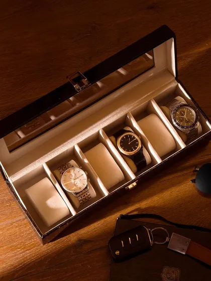 An overhead shot of a watch collection box on a wooden surface. The play of light and shadow adds a dramatic, premium feel, perfect for luxury accessory brands.
