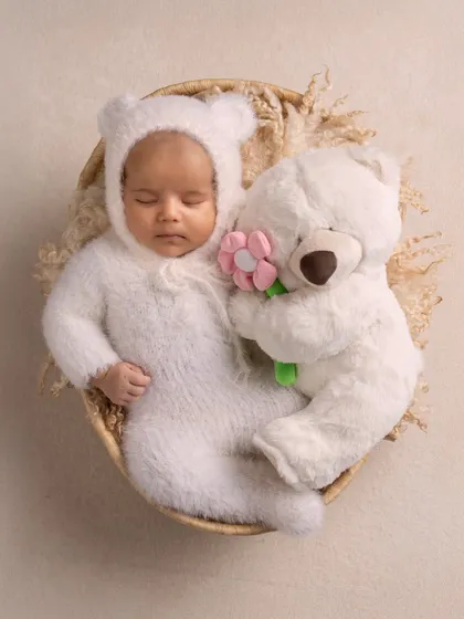 A sweet, sleeping newborn dressed as a tiny bear, cuddling with a teddy. This artistic portrait shows how we can use simple props to create a magical and adorable scene.