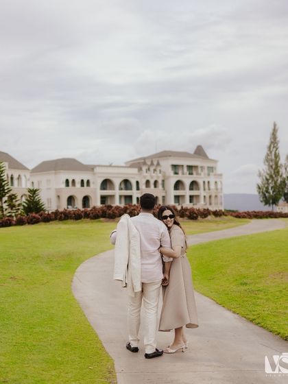A couple walking away from the camera through the lush grounds of a castle-like building in Thailand. This candid-style shot feels natural and tells a story of a shared journey.