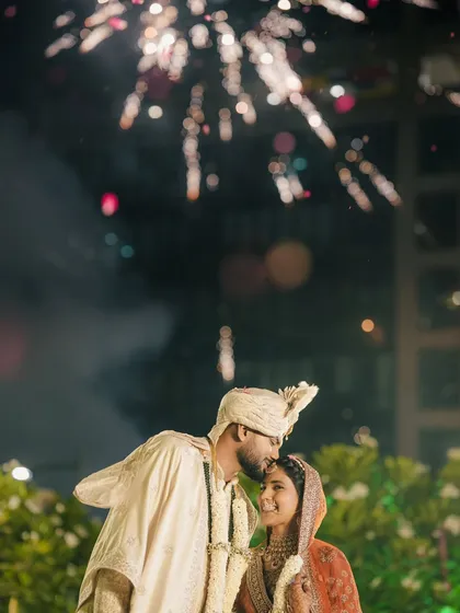 A magical moment captured with fireworks in the background. The groom's gentle kiss on the bride's forehead is a perfect post-varmala shot.