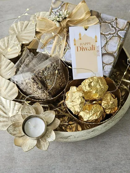 I designed this hamper for a rustic, earthy feel. Set in a wooden bowl, it contains a floral T-light holder, packets of healthy snacks, and Ferrero Rocher chocolates, all tied together with twinkling fairy lights.