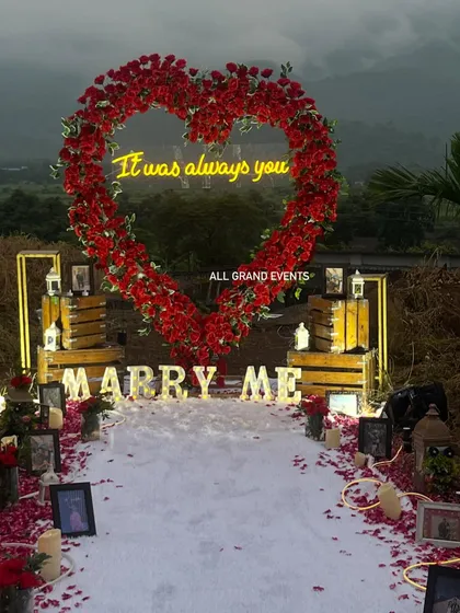 For a truly unforgettable moment, we designed this grand outdoor proposal setup. The centerpiece is a stunning heart-shaped arch made of hundreds of red roses, with a custom neon sign saying 'It was always you'. The aisle is lined with a white carpet, scattered rose petals, and framed photos, creating a personalized journey to the big question.