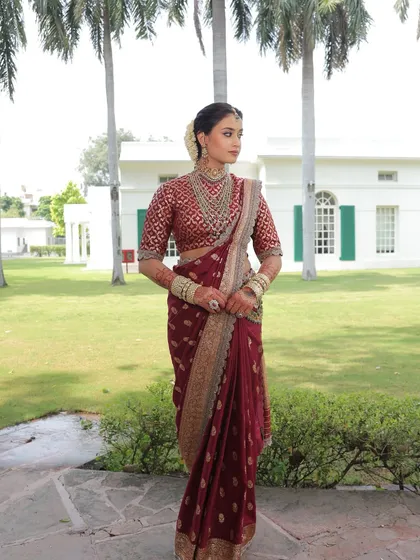 A full-length shot of the bride in her maroon saree, exuding grace and elegance in a beautiful garden setting.