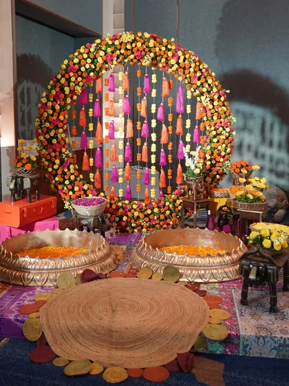 A Haldi ceremony is all about vibrant joy. This setup features a circular backdrop of marigolds and colorful tassels, with traditional brass urlis filled with petals, creating a festive and picture-perfect space for the ritual.