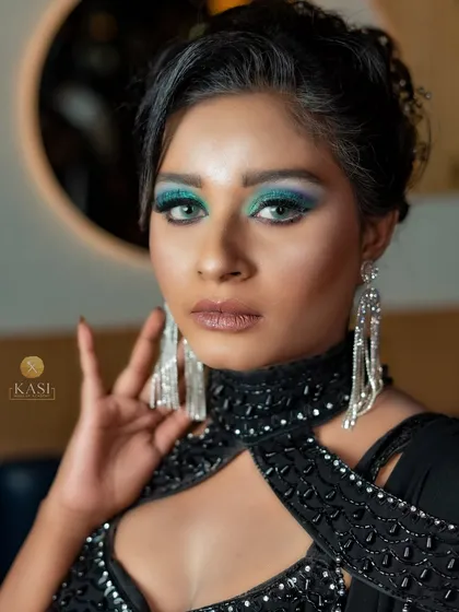 A close-up of a glamorous black-on-black look. The pop of blue-green glitter on the eyes is the star.