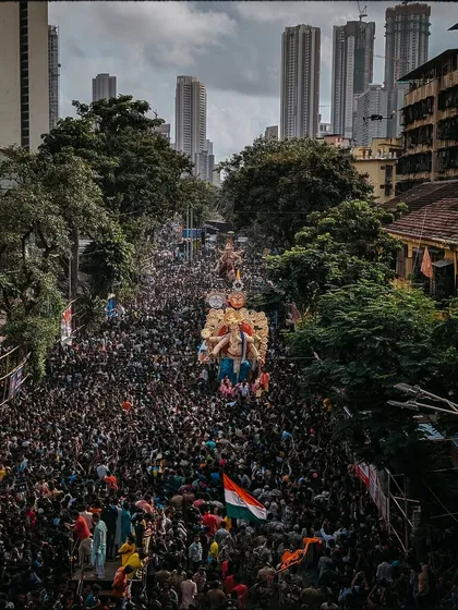 A drone's view of the procession snaking through the city, with modern skyscrapers in the background, creating a contrast between tradition and urban life.