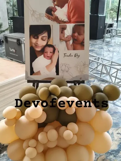 A personalized welcome easel sign for a baby's celebration. The sign features a collage of the baby's photos and is decorated with a cluster of balloons matching the party's earthy color scheme.