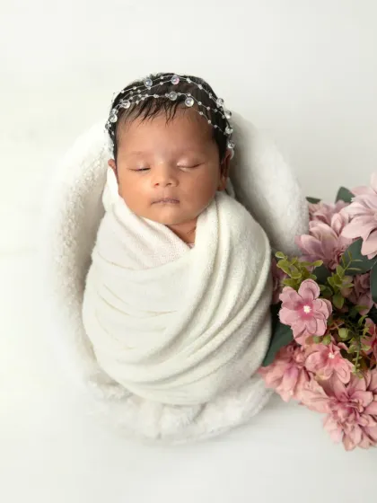 There is so much beauty in simplicity. This portrait showcases a peacefully sleeping newborn, swaddled in pure white and adorned with a delicate crystal headband. It’s a timeless and angelic look that focuses entirely on your baby.