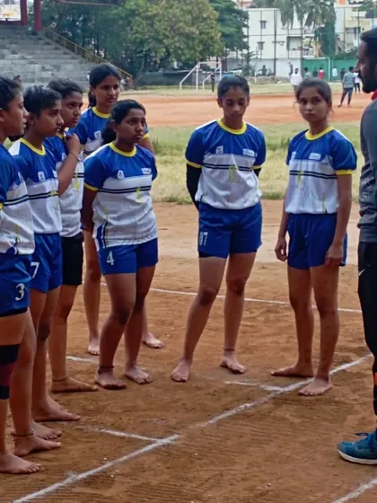 A coach giving strategic advice to the girls' Kabaddi team during a break in their practice match.
