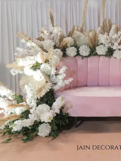 A plush pink sofa becomes a piece of art with a cascade of white pampas grass and florals. This is how I turn a simple seating element into a statement photo booth.