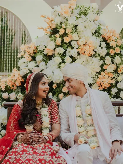 A sweet moment between the bride and groom as they sit together amidst beautiful floral decor. Their shared glance and smiles tell a story of happiness and love.