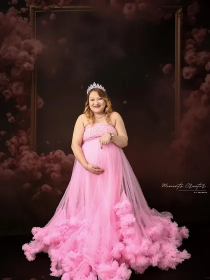 A princess moment. The mom-to-be wears a tiara and a beautiful pink tulle gown, creating a magical and celebratory portrait against a cloudy, dramatic backdrop.