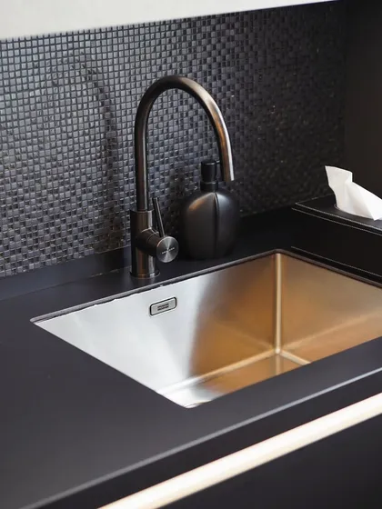 The sink and faucet detail in the Mibu Residence kitchen. The matte black finish of the countertop continues seamlessly, paired with a durable stainless steel sink for a practical yet stylish wet area.