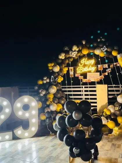 An outdoor 29th birthday party on a terrace. This nighttime setup features a circular balloon arch, a neon sign, and large marquee numbers.